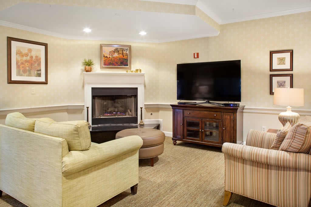 A cozy living room featuring a fireplace and modern furnishings, with a large television on a wooden stand.