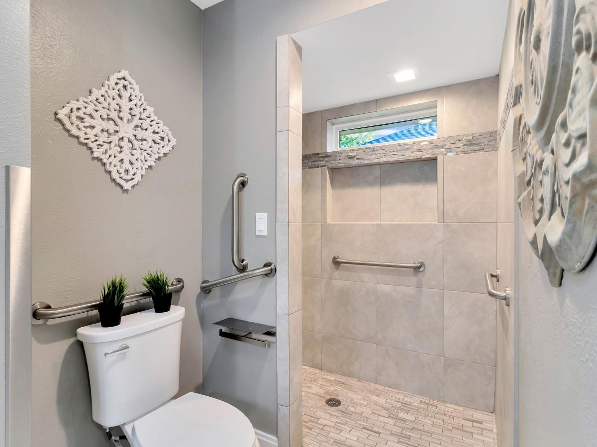 A modern bathroom featuring a walk-in shower with grab bars and a simple decorative touch.