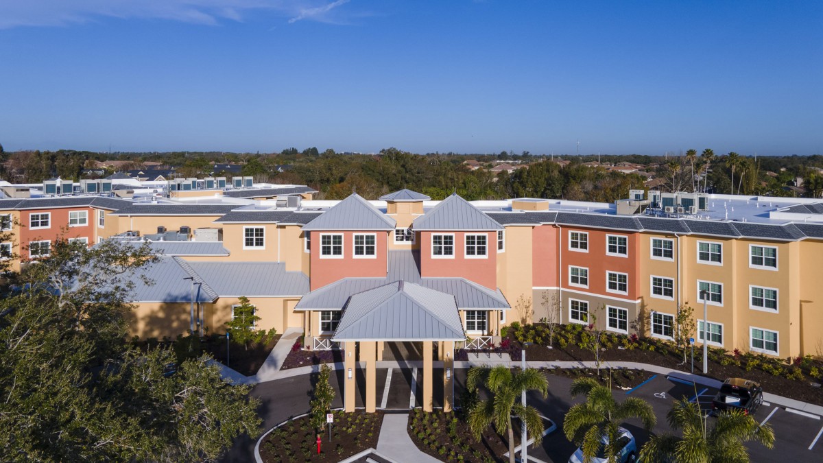 Aerial view of a modern building with a landscaped entrance and clear blue sky.