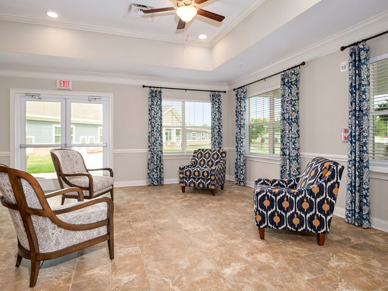 A cozy seating area with patterned armchairs and a ceiling fan in a bright room.