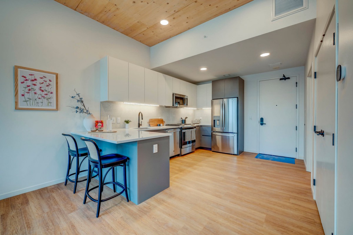 A modern kitchen with stainless steel appliances and a minimalist design, featuring a breakfast bar and wood flooring.