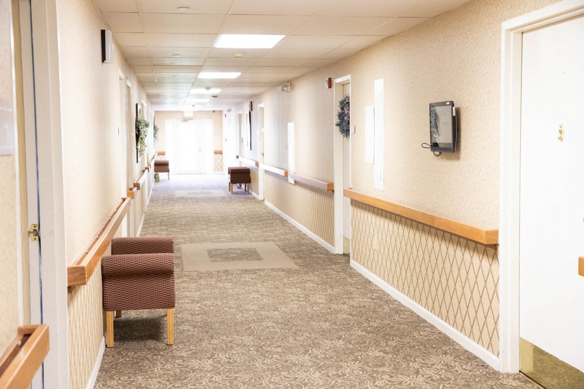 A bright, carpeted hallway with seating and light fixtures in a care facility.