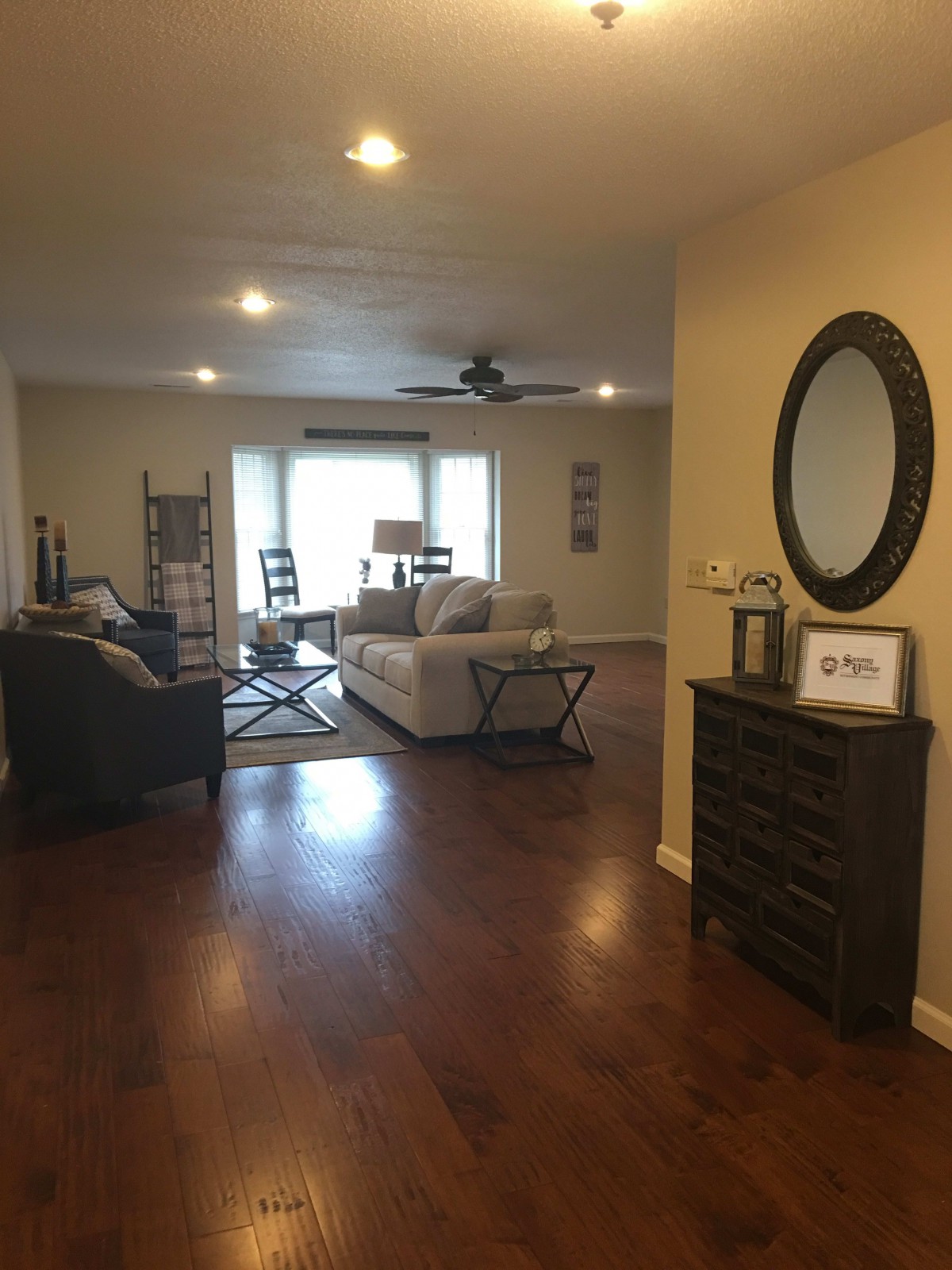 A spacious living room with a sofa set, hardwood floors, and a decorative mirror.