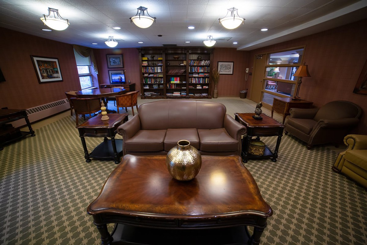 A cozy library reading room featuring bookshelves, a sofa, and wooden tables with decor.