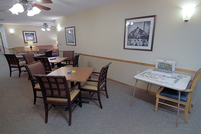 A dining area with several tables and chairs, featuring wall artwork and a carpeted floor.