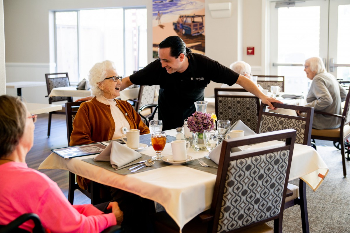 A man engages in a friendly conversation with an elderly woman in a dining area.