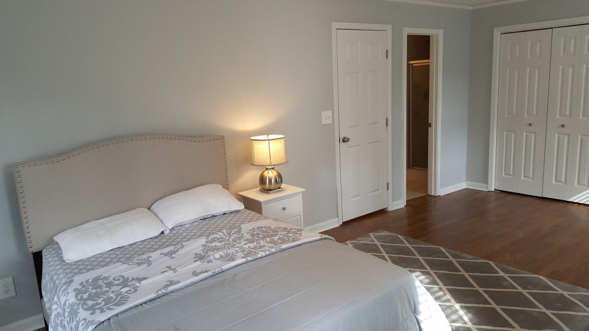 A cozy bedroom featuring a neatly made bed, a nightstand with a lamp, and an open door leading to another room.