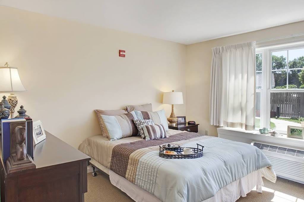A cozy bedroom with a neatly made bed, pillows, and a bedside lamp near a window with curtains.