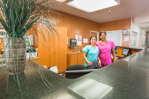 Two staff members pose at a reception desk in a healthcare setting.