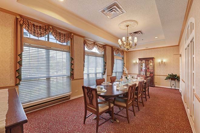 An elegant dining room with a long table set for a meal, surrounded by chairs and illuminated by a chandelier.