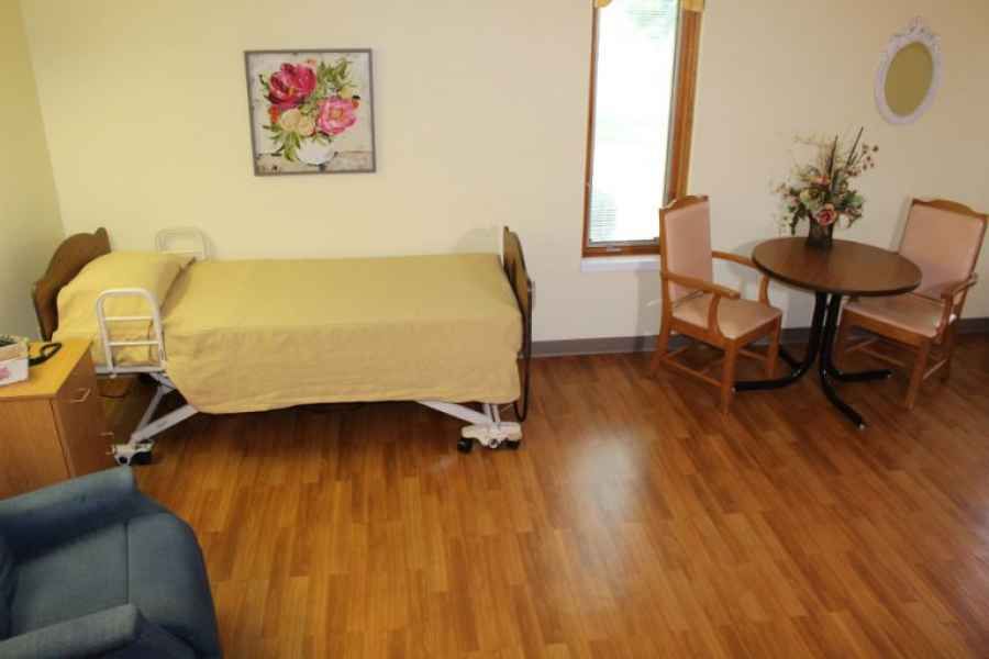 A simple bedroom with a hospital bed, wooden floor, and minimal furniture.