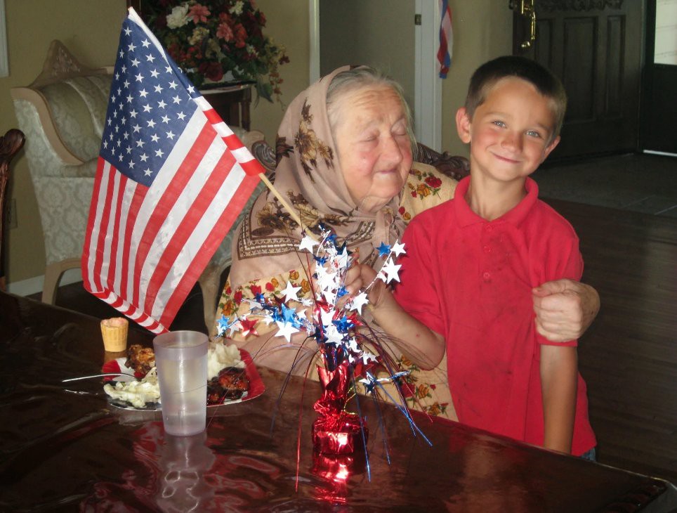 An elderly woman and a young boy smiling with an American flag decoration on the table.