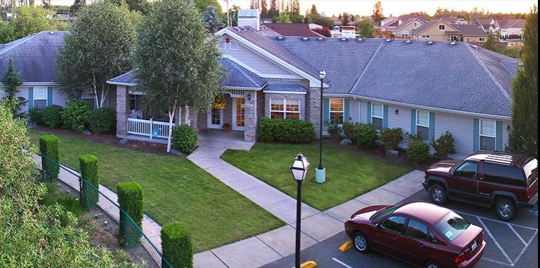 A residential house with a well-maintained lawn and driveway, featuring a parked car and a lamp post.