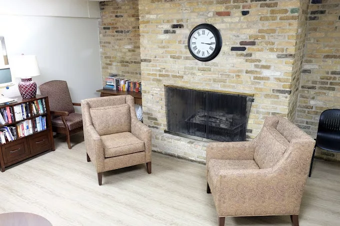 A cozy seating area featuring a brick fireplace, two armchairs, and a clock on the wall.