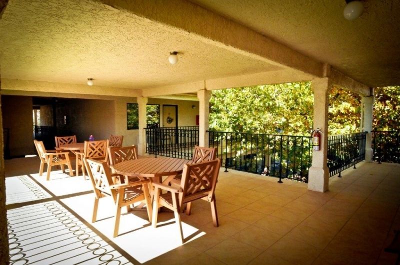 A spacious outdoor patio with wooden tables and chairs, shaded by a canopy.
