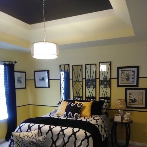 A modern bedroom with yellow walls, featuring black and white bedding and stylish wall art, illuminated by a pendant light.
