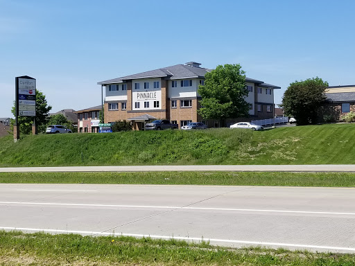 A commercial building visible from the roadside, surrounded by greenery under a clear blue sky.