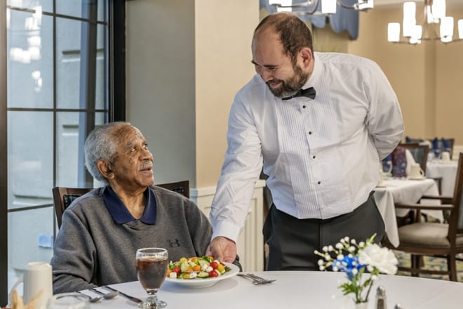 A waiter serves a meal to an elderly person at a restaurant.