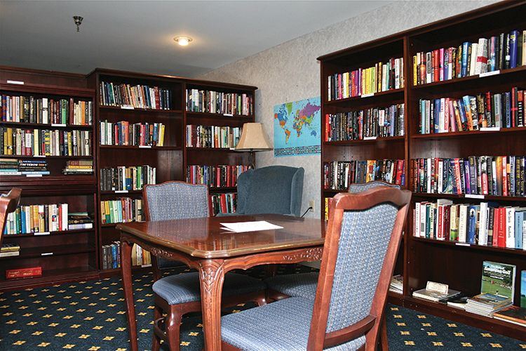 A cozy library room with wooden bookshelves filled with books, a central table, and comfortable chairs.