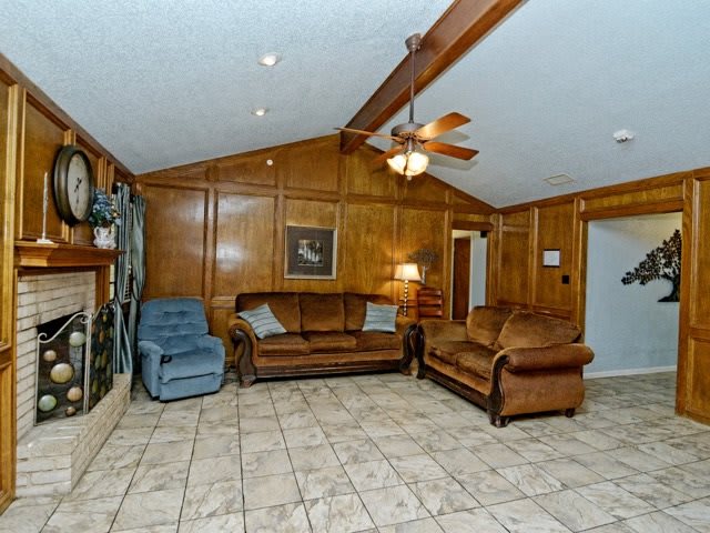 A cozy living room with wood paneling, featuring a ceiling fan, two leather sofas, a recliner, and tiled flooring.