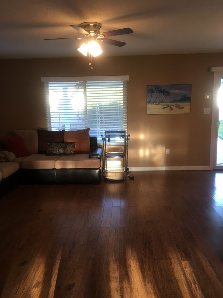 A cozy living room with wood flooring, a large couch, and a painting on the wall, illuminated by natural light through the window.