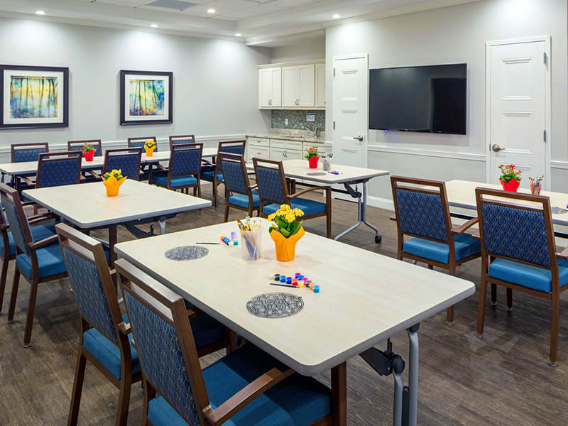 A modern classroom setup with tables and chairs, featuring a television and decorative elements.
