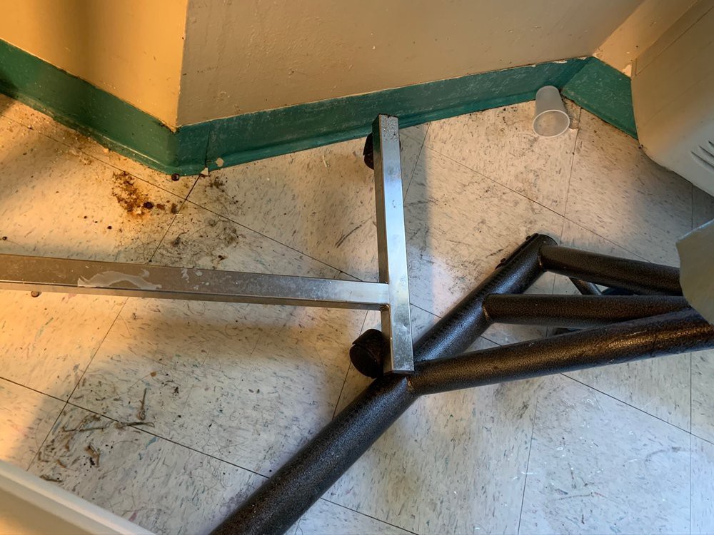 A broken metal furniture frame lying on a dirty floor in the corner of a room.