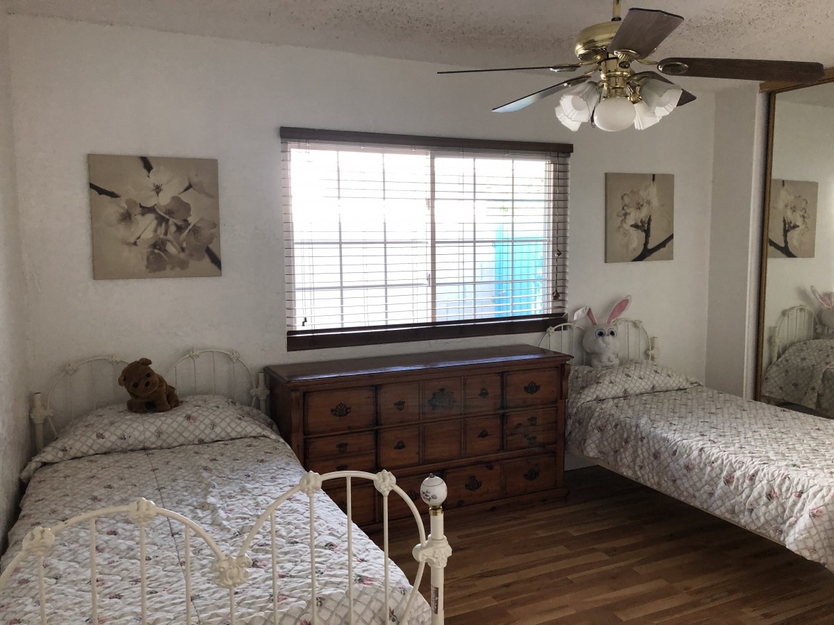 A cozy bedroom with twin beds and a wooden dresser beneath a window, featuring a ceiling fan and floral decor.