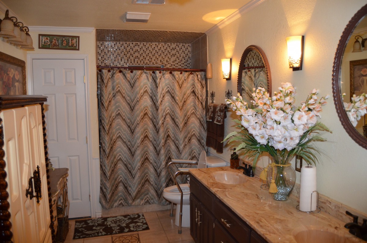 A well-decorated bathroom featuring a patterned shower curtain, a wooden vanity with a large mirror, and elegant lighting fixtures.