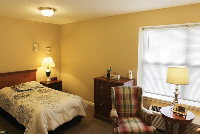 A cozy bedroom featuring a bed, dresser, and an armchair near the window.