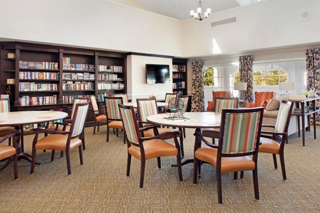 A cozy library room with bookshelves, multiple tables and chairs, and a television on the wall.