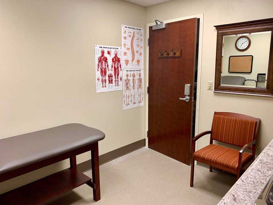 A typical doctor's examination room featuring an exam table, chair, and medical posters on the wall.