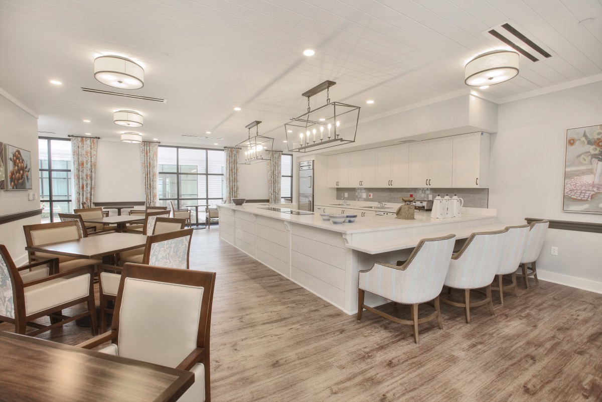 A spacious, modern kitchen with an island counter and dining area, featuring elegant chandeliers and wood flooring.