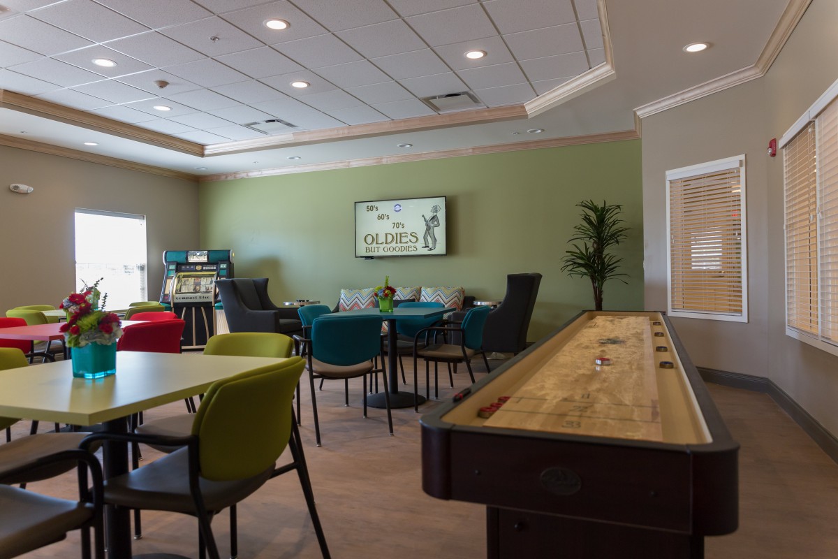 A community recreation room with tables, chairs, and a shuffleboard table.