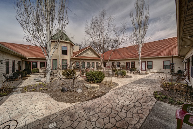 A serene courtyard with a stone pathway and red-roofed buildings under a cloudy sky.
