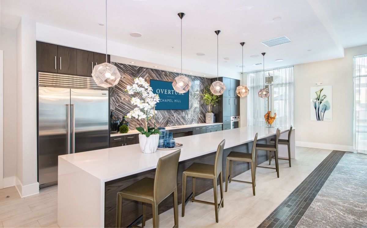 A modern kitchen with stylish pendant lighting, bar stools, and decorative tile backsplash.
