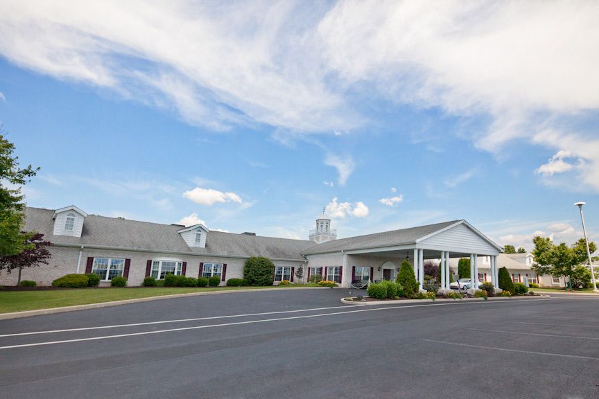 A single-story building with a large parking area, set against a blue sky with scattered clouds.