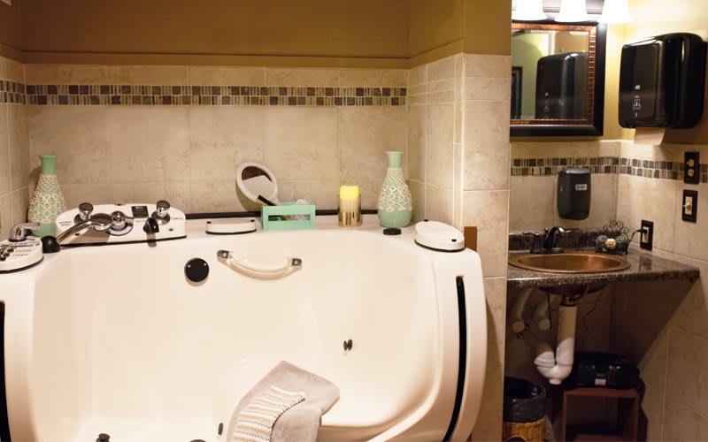 A cozy bathroom featuring a large bathtub surrounded by decorative tiles, with various toiletries and towels neatly arranged.