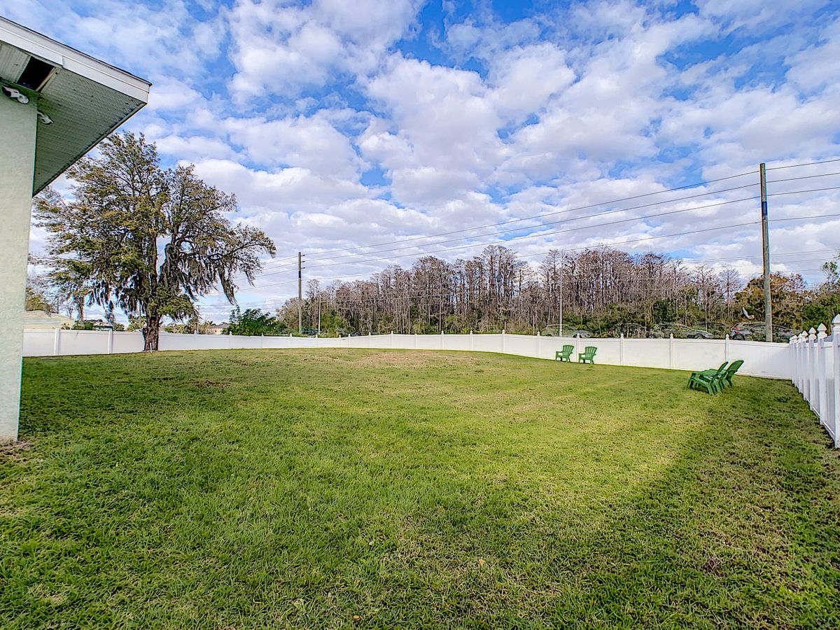 A spacious grassy yard with a tree, bordered by a fence under a partly cloudy sky.