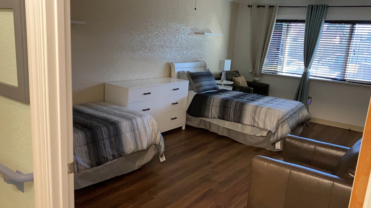 A cozy bedroom with two beds, a dresser, and a window letting in natural light.