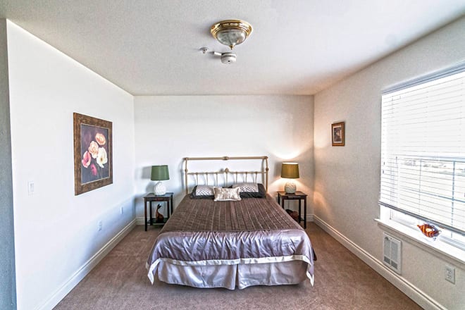 A cozy bedroom with a metal-framed bed, two side tables with lamps, and artwork on the walls.