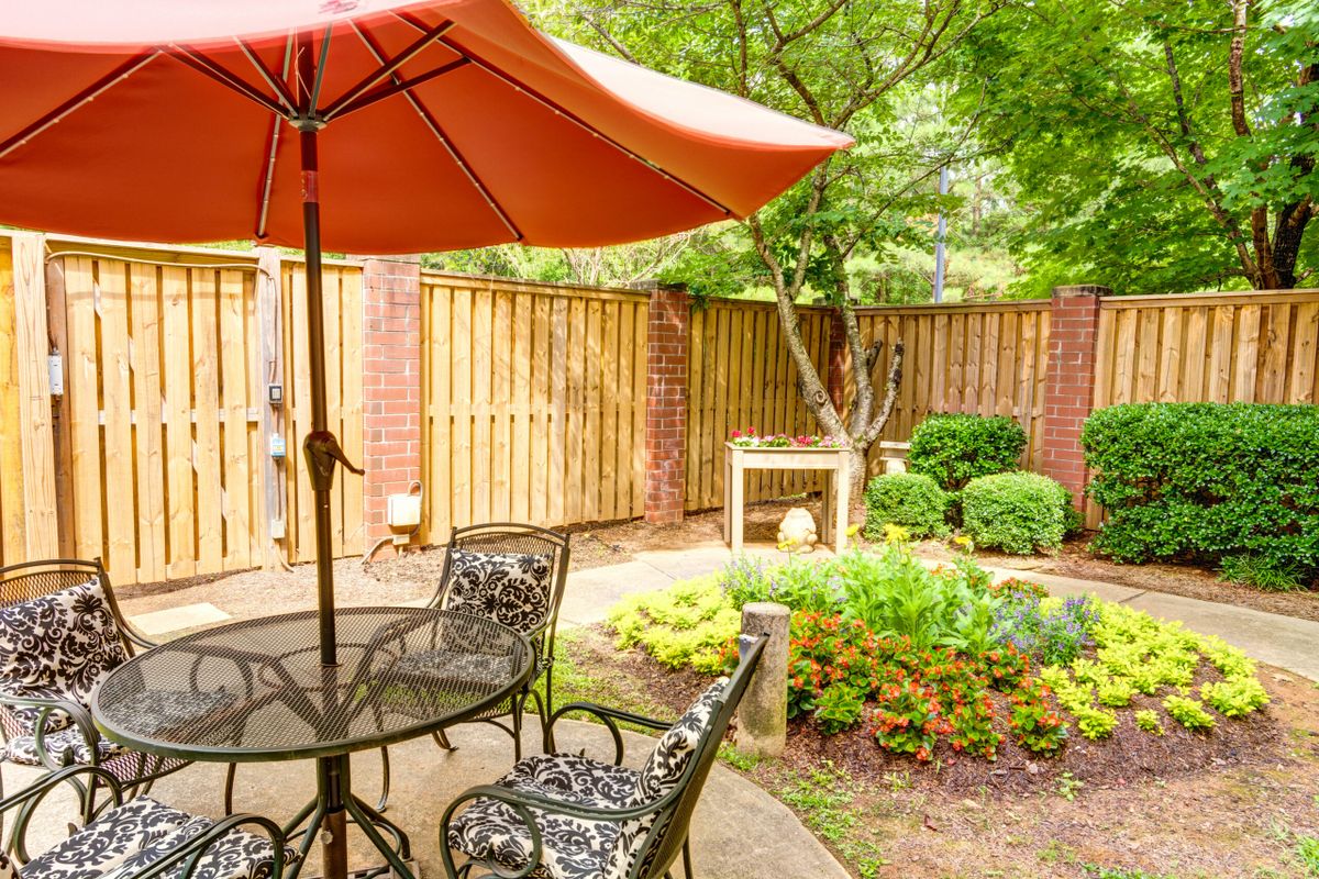 A cozy patio area with a table, chairs, and an umbrella surrounded by a garden.