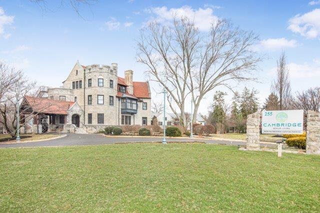 A historic stone mansion with a large lawn and towering trees, set against a clear blue sky.
