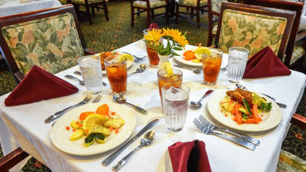 A beautifully set dining table with plates of food, iced tea, and neatly arranged cutlery.