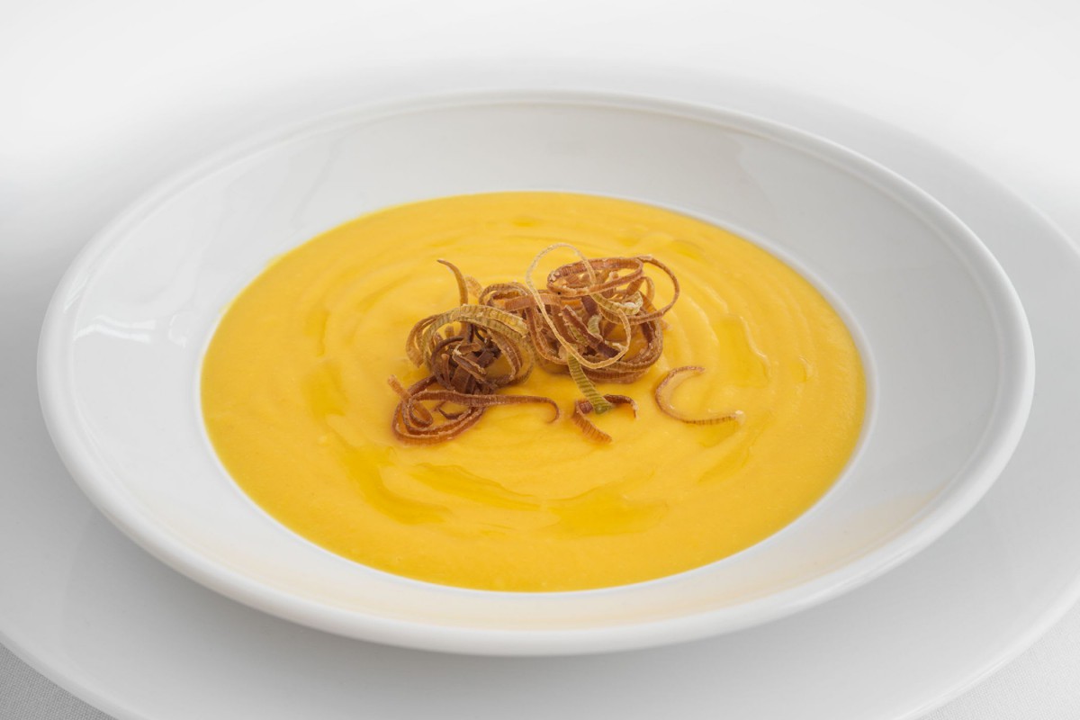 A creamy pumpkin soup garnished with crispy fried onions.