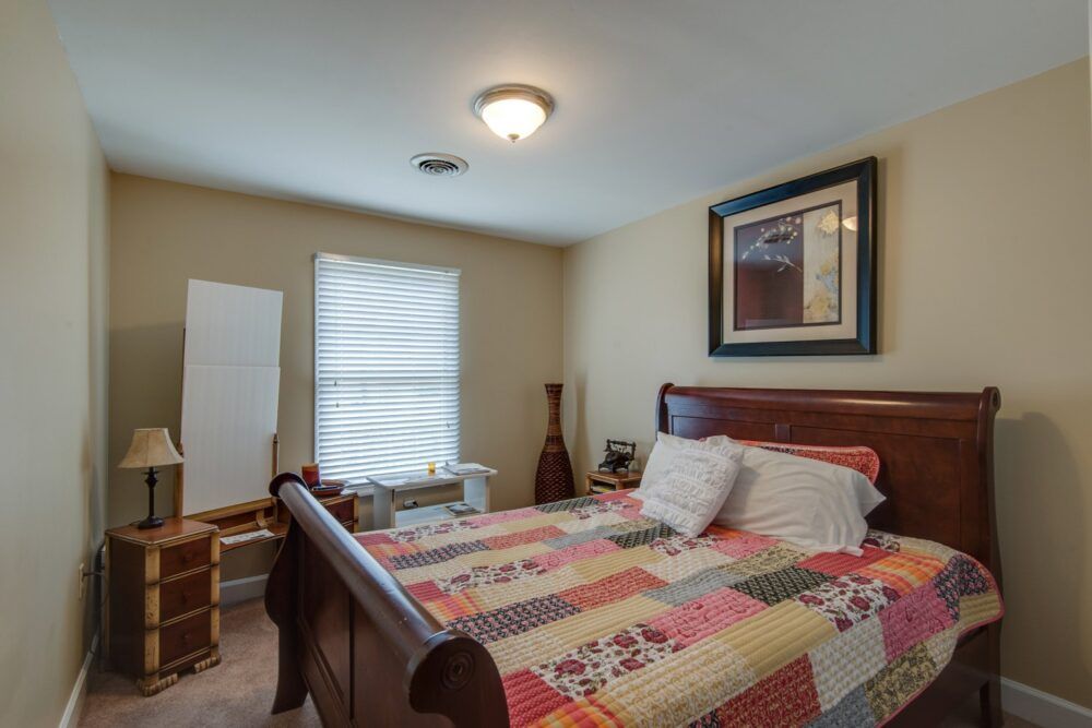 A cozy bedroom with a colorful quilt on the bed and framed artwork on the wall.