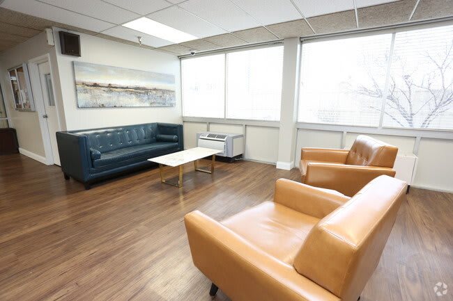 A modern waiting room with sofas, chairs, and a coffee table in a well-lit office space.