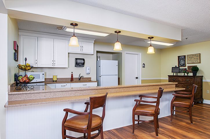 A well-lit kitchen with a wooden counter and chairs, featuring pendant lighting and modern appliances.