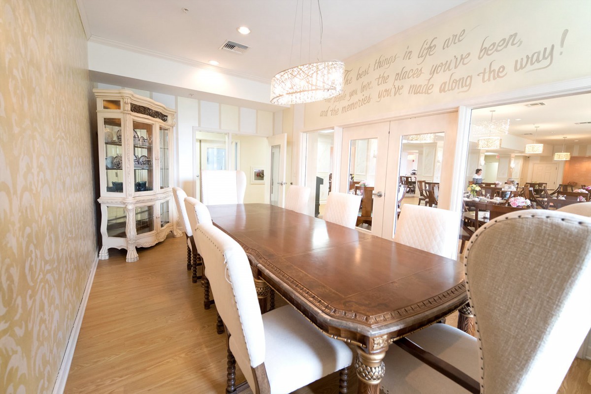 An elegant dining room with a long wooden table, upholstered chairs, and a chandelier.