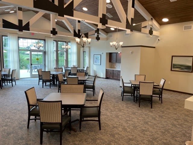 A spacious dining area featuring multiple tables and chairs, with chandeliers and large windows providing natural light.